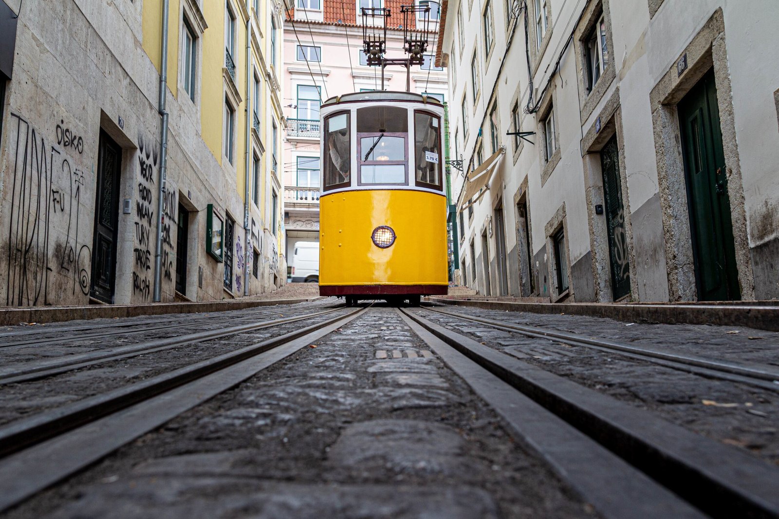 a yellow tram going down a narrow alley surrounded by old buildings